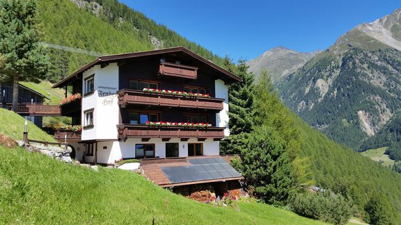 A cozy building in the mountains, surrounded by green meadows and trees. Majestic mountains are visible in the background. - Appartementhaus Fenderhof - Sölden | © Sommerbild