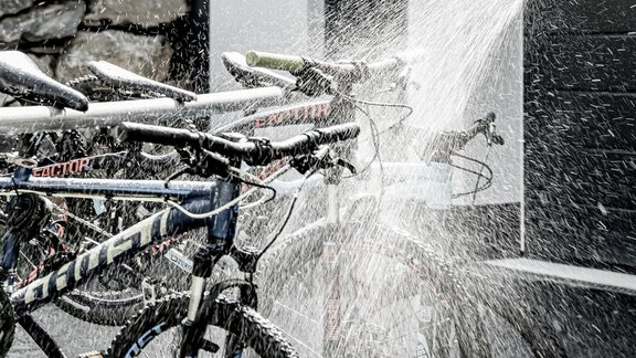 Two mountain bikes are being sprayed with water. The bicycles are standing on an asphalt floor in front of a wall. - Appartementhaus Kathrin - Sölden