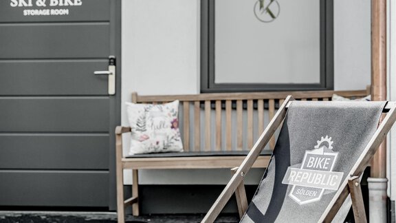 A cozy outdoor area with a deck chair and a wooden bench. The walls display signs for "Ski & Bike". - Appartementhaus Kathrin - Sölden