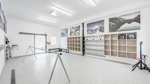 A bright and spacious room with white walls and a shiny floor. Pictures of mountains hang on the walls, and there are shelves for storage. - Appartementhaus Kathrin - Sölden