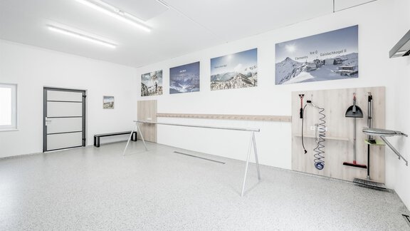 A modern room with bright walls and a shiny floor. The walls are adorned with pictures of mountain landscapes, and there are practical shelf spaces and tools. - Appartementhaus Kathrin - Sölden