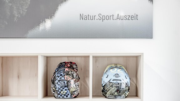 Two backpacks are standing on a shelf with a wall painting in the background. The text on the painting reads: "Nature.Sport.Break." - Appartementhaus Kathrin - Sölden