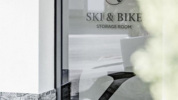 A modern door with a glass window displaying the logo "Ski & Bike Storage Room." The entrance area is designed to be simple and inviting. - Appartementhaus Kathrin - Sölden