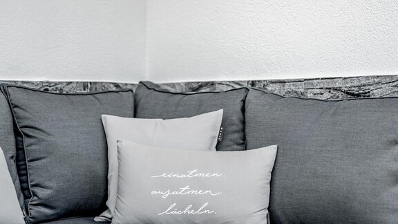 A modern sofa with gray cushions and a small table. On the table, there is a flower decoration. - Appartementhaus Kathrin - Sölden