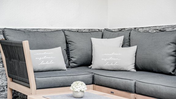 A cozy seating area with gray cushions and a small table. The background looks modern and inviting. - Appartementhaus Kathrin - Sölden