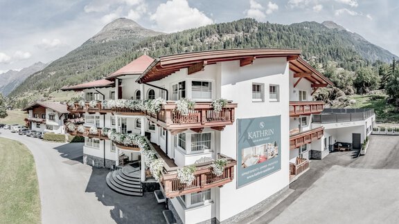 A modern building in alpine style with several balconies. In the background, green mountains and a clear sky can be seen. - Appartementhaus Kathrin - Sölden