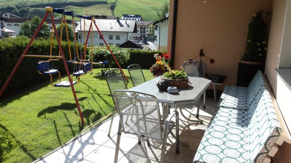 A cozy balcony with a table, chairs, and a bench. In the background, there is a playground swing, and the green landscape is visible. - Appt. Ideal - Sölden