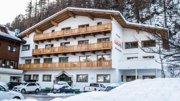 A modern hotel in winter with snow-covered ground. The facade is bright and has wooden balconies. - Gästehaus Europa - Sölden