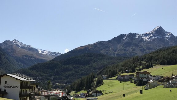 A picturesque mountain landscape with snow-covered peaks. In the foreground, green meadows and a charming village lie. - Gästehaus Martin - Sölden