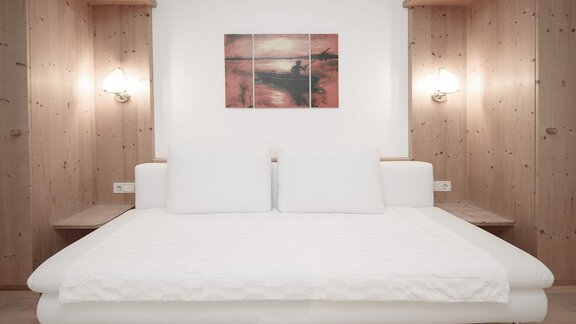 A modern bedroom with a white bed and wood paneling. An abstract artwork hangs on the wall. - Haus Ingrid - Sölden