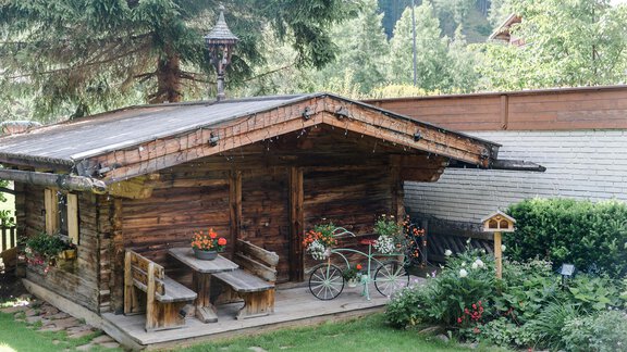 A rustic wooden cabin with a cozy seating area outdoors. Surrounded by colorful flowers and green grass. - Hotel Sportpension Carinthia - Sölden