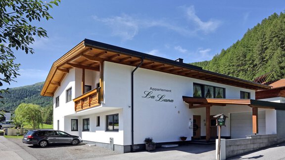 A modern apartment building with wooden cladding in a quiet environment. The facade is bright and inviting, surrounded by green mountains and trees. - La Luna - Sölden