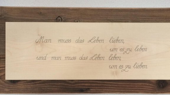 Ein Holzschild mit einer handgeschriebenen Botschaft über das Leben. Der Text besagt, dass man das Leben lieben muss, um es zu leben und zu lieben. - La Luna - Sölden
