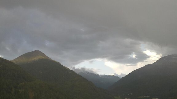 Eine malerische Berglandschaft unter einem bewölkten Himmel. Im Vordergrund sind grüne Hügel und ein kleines Dorf zu sehen. - La Luna - Sölden