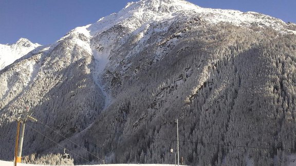 Ein majestätischer verschneiter Berg mit dichten Wäldern im Vordergrund. Der klare Himmel und die winterliche Landschaft laden zum Skifahren ein. - La Luna - Sölden