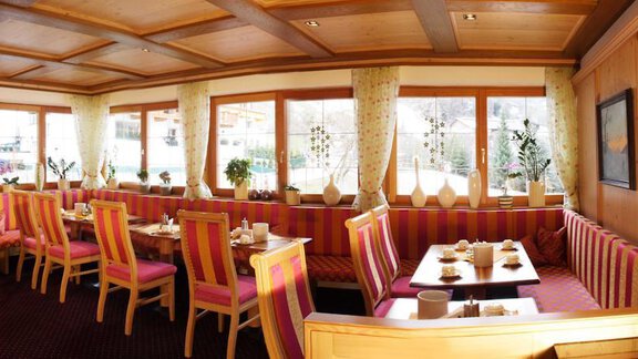 A cozy restaurant with wooden ceilings and colorful chairs. Large windows let in plenty of light and offer a view of the surroundings. - Pension Sportalm - Sölden