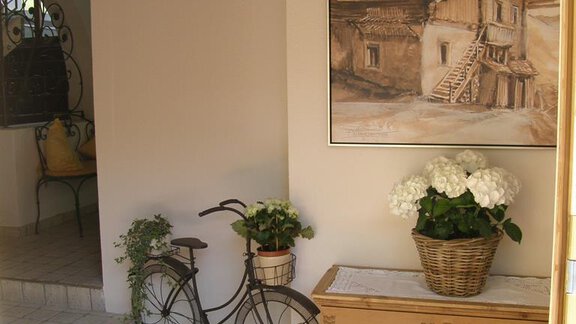 An inviting entrance area with a wire bicycle and a painted landscape. Flowers in pots and a decorative carpet complete the ambiance. - Pension Sportalm - Sölden