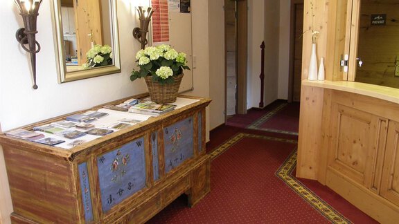 An inviting hallway with a decorative wooden cabinet and green plants. The walls are bright, and the floor has a red carpet. - Pension Sportalm - Sölden