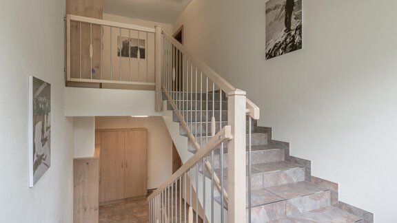 A bright hallway with a staircase and wooden railing. Some pictures are hanging on the walls. - Residenz Allegra - Sölden | © Residenz Allegra Sölden