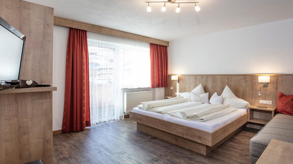 A modern room with a double bed and a cozy seating area. Large windows and warm colors create an inviting atmosphere. - Sportpension Rubin - Sölden
