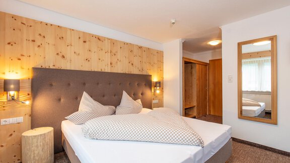 A modern bedroom with a large bed and cozy furnishings. Particularly noteworthy is the wooden paneling on the wall and the large mirror. - Vizensn Living - Sölden