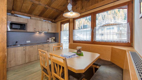 A cozy kitchen with wooden elements and a dining area. Large windows let in plenty of light and offer a view of the surrounding mountains. - Vizensn Living - Sölden