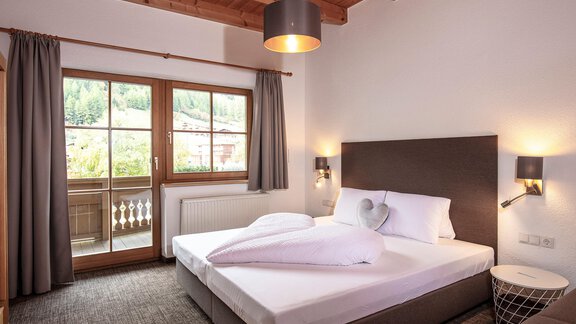A cozy bedroom with a large bed and a wooden ceiling. The window offers a beautiful view of nature outside. - Vizensn Living - Sölden