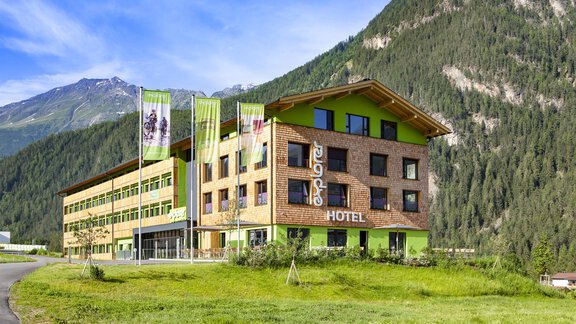 Das Explorer Hotel Ötztal präsentiert hier die Außenansicht im Sommer. Im Hintergrund kann man die Ötztaler Alpen sehen. - Umhausen