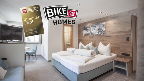 A modern hotel room with a large bed and cozy decor. In the foreground, the summer menu and the logo of Bike Homes are visible. - Garni Ötztal ROOMS & APARTS - Zwieselstein