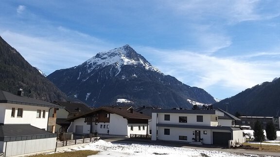 Eine malerische Berglandschaft mit schneebedecktem Gipfel und einem klaren blauen Himmel. Im Vordergrund sind verschiedene Häuser und Wiesen zu sehen. - Apart Katja - Längenfeld