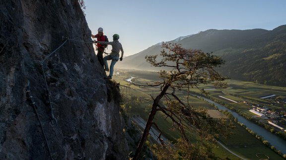 Zwei Kletterer erklimmen eine steile Felswand in einer malerischen Berglandschaft. Im Hintergrund fließt ein Fluss durch das grüne Tal unter einem klaren Himmel. - Gasthof Waldesruh - Ochsengarten