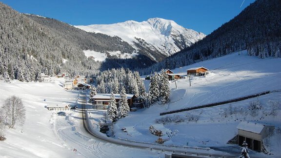 Eine winterliche Berglandschaft mit schneebedeckten Hügeln und charmanten Chalets. Im Hintergrund ist ein hoher, schneebedeckter Gipfel zu sehen. - Gasthof Waldesruh - Ochsengarten