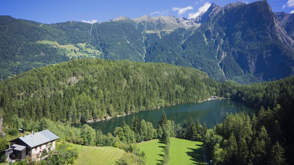 Eine malerische Landschaft mit einem klaren See, umgeben von grünen Wäldern und Bergen. Im Vordergrund ist ein charmantes Haus sichtbar. - Gasthof Waldesruh - Ochsengarten