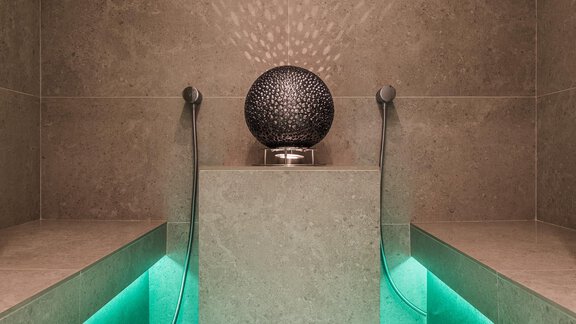 An elegant spa area with a modern water source and soft lighting. The walls are lined with gray tiles, and the lighting effects create a relaxing atmosphere. - Andre Arnold - Boutique Hotel - Sölden