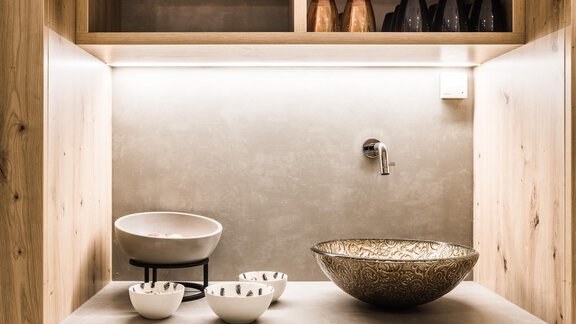 A modern kitchen unit with an elegant sink and various bowls. The wooden shelves are stylish and well-lit. - Andre Arnold - Boutique Hotel - Sölden