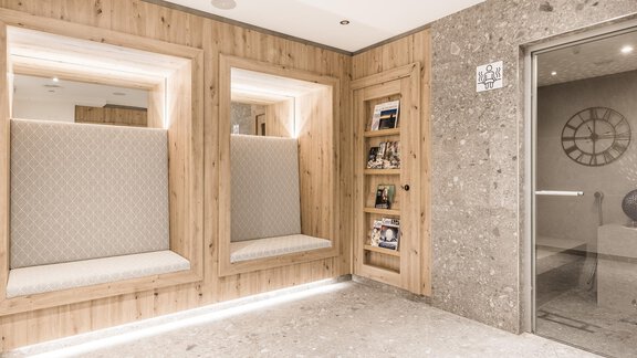 A modern entrance area with wooden paneling and elegant seating niches. The walls are designed with gray stones and there is a large glass wall that floods the room with light. - Andre Arnold - Boutique Hotel - Sölden