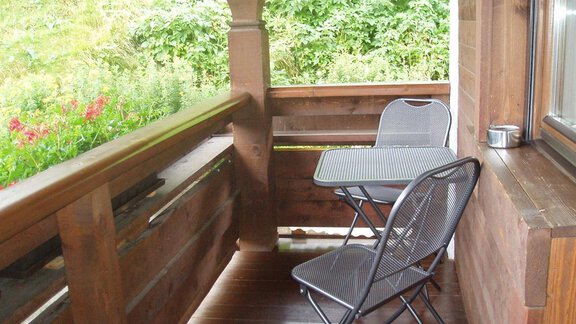 A cozy balcony with a small table and two chairs. The surroundings are green and lush, ideal for relaxing moments outdoors. - Appartement Harmonie - Sölden