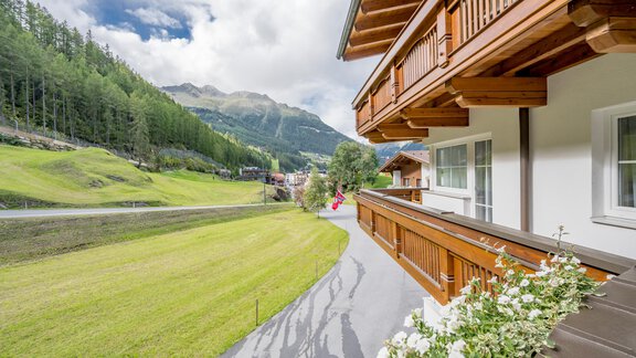 A picturesque view from a balcony over green meadows and surrounding mountains. The sky is cloudy, and there are scattered trees in the background. - Appartementhaus Kathrin - Sölden