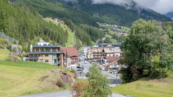A picturesque alpine landscape with a small village and modern buildings. In the background, green hills and clouds can be seen. - Appartementhaus Kathrin - Sölden