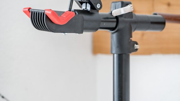 A tripod with a holder that is red and black. It is in a bright room with a wooden surface in the background. - Appartementhaus Kathrin - Sölden