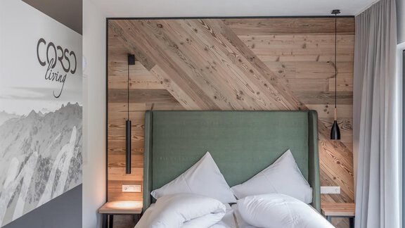A modern bedroom with a green headboard and white pillows. The wall is made of wood panels and features a minimalist design. - CORSO living Aparthotel - Sölden