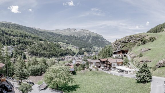 A beautiful mountain landscape with green meadows and wooded hills. In the foreground, several buildings are visible, embedded in nature. - CORSO living Aparthotel - Sölden