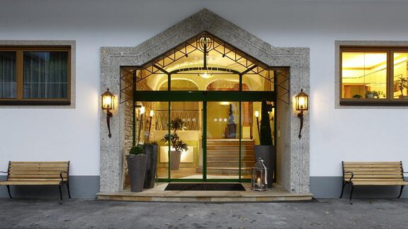 Entrance to a stylish hotel with large windows and an inviting atmosphere. Benches are positioned on both sides of the entrance. - Gästehaus Europa - Sölden
