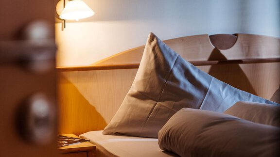 A cozy bedroom with a large pillow and a gray blanket. The light is warm and inviting, perfect for relaxing. - Gästehaus Europa - Sölden