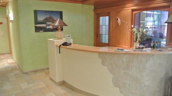 A reception desk in a bright, friendly room. The walls are painted in soft colors, and a picture as well as plants decorate the area. - Gästehaus Europa - Sölden