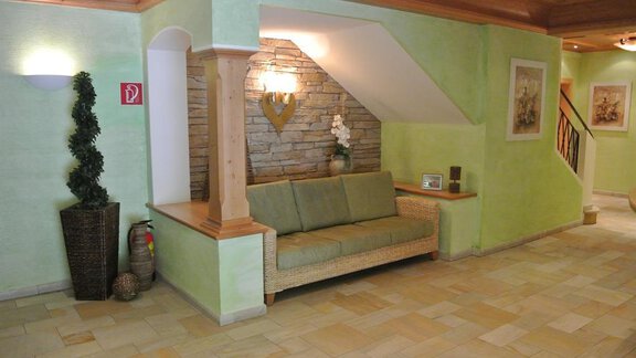 A cozy interior with a green sofa and a stone wall. On the left, there is a plant in a corner and the room has warm lighting. - Gästehaus Europa - Sölden