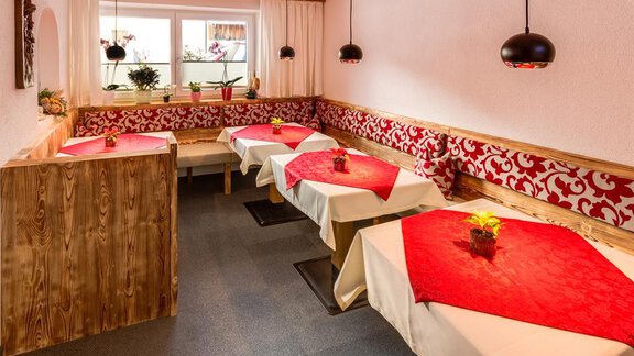 A cozy restaurant with red tablecloths and wooden benches. Large windows let in plenty of light. - Haus Edmund - Sölden