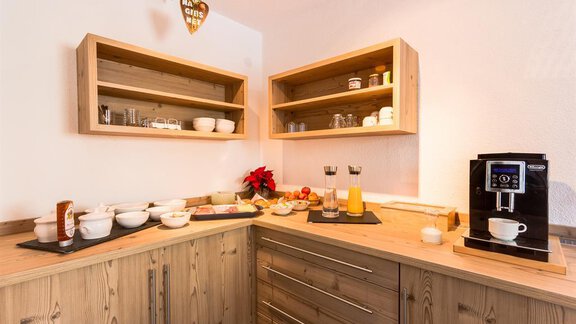 A cozy kitchen corner with wooden shelves and a coffee machine. There are various food items and drinks on the table, perfect for breakfast. - Haus Edmund - Sölden