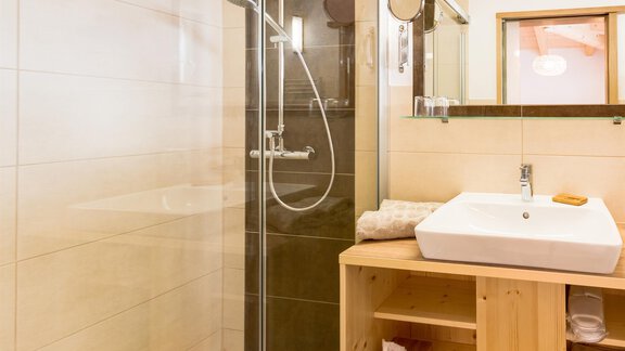 A modern bathroom with a stone shower and sink. The walls are light tiled, and wooden shelves provide additional storage space. - Haus Edmund - Sölden