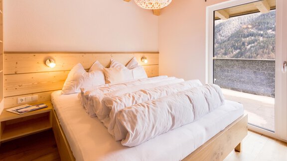 A modern bedroom with a large bed and wood décor. On the wall, there is a window overlooking the mountains. - Haus Edmund - Sölden